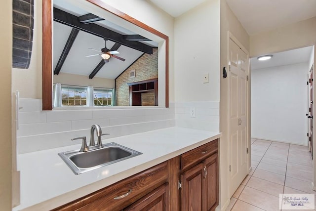 kitchen featuring light tile patterned floors, brown cabinets, vaulted ceiling with beams, light countertops, and a sink