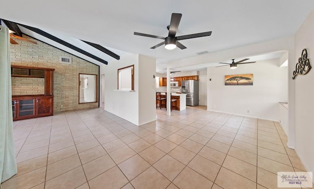 unfurnished living room featuring ceiling fan, vaulted ceiling with skylight, light tile patterned flooring, brick wall, and visible vents