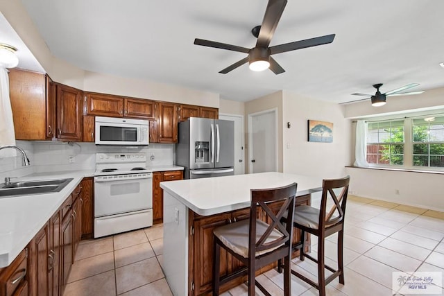 kitchen featuring a breakfast bar, light tile patterned floors, tasteful backsplash, a sink, and white appliances