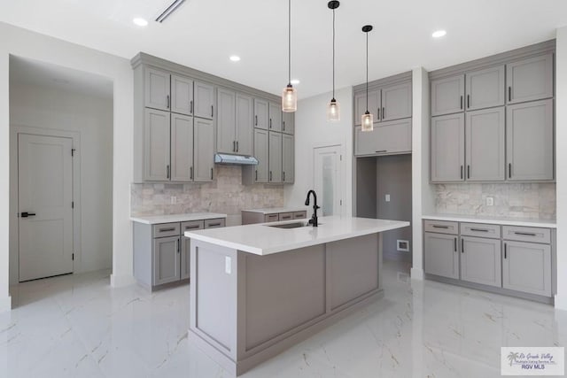 kitchen featuring backsplash, a kitchen island with sink, sink, gray cabinets, and decorative light fixtures