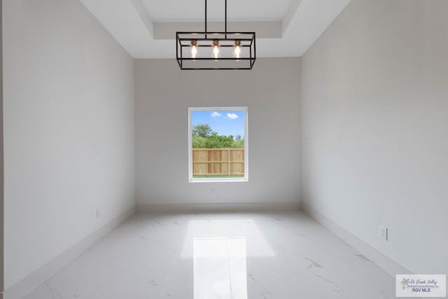 spare room featuring a raised ceiling and a notable chandelier