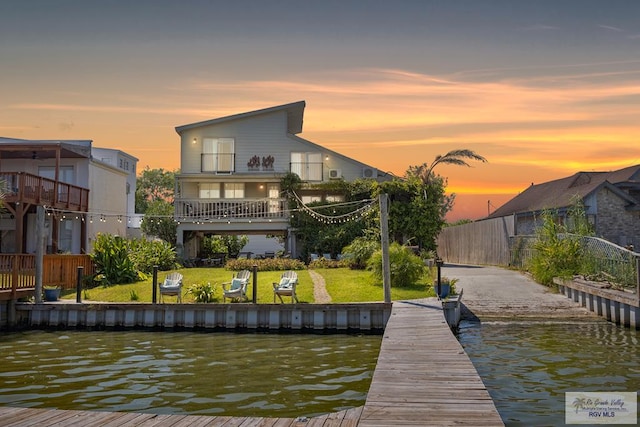 back of property at dusk featuring a lawn, a water view, and fence