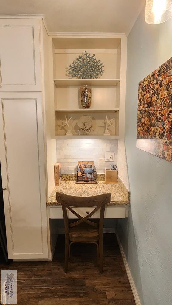 interior space featuring ornamental molding, built in desk, dark wood-style flooring, and baseboards