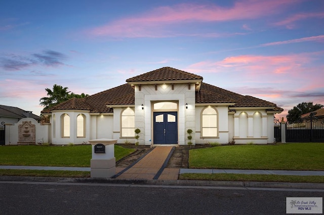 mediterranean / spanish-style house featuring stucco siding, a tile roof, fence, and a front yard