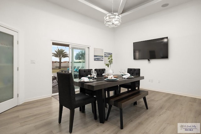 dining room with light wood-type flooring, a raised ceiling, and baseboards