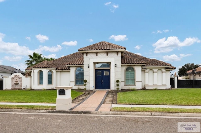 mediterranean / spanish-style home with a front lawn, a tile roof, and fence