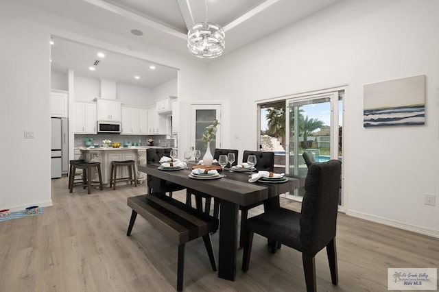 dining space with light wood-style floors, baseboards, a tray ceiling, and a chandelier