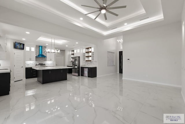 kitchen featuring tasteful backsplash, a raised ceiling, a kitchen island, stainless steel appliances, and wall chimney range hood