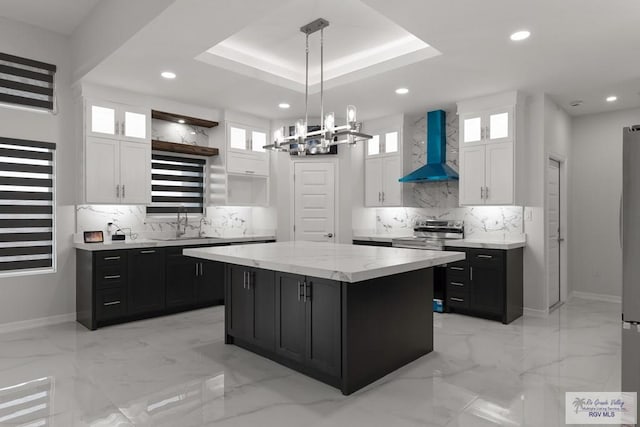 kitchen with a center island, a tray ceiling, white cabinets, pendant lighting, and wall chimney range hood