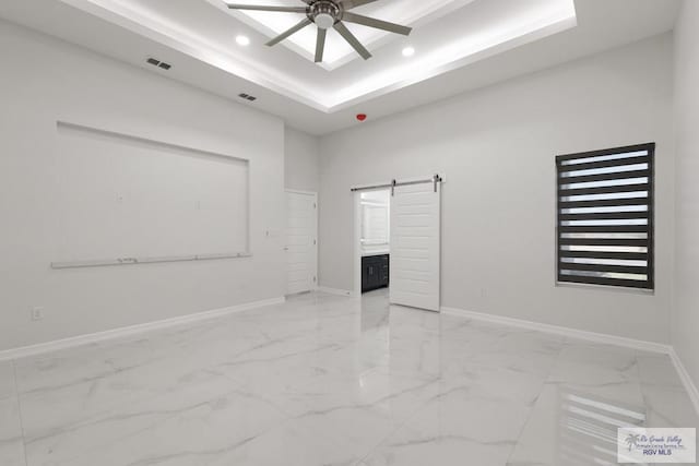 unfurnished room with a raised ceiling, a barn door, and ceiling fan