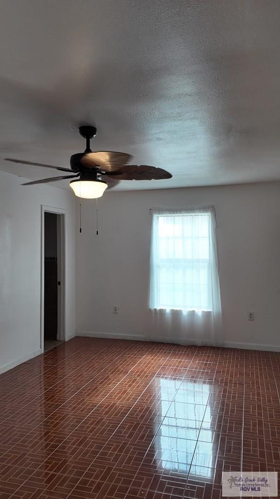 spare room with a ceiling fan and baseboards