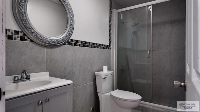 full bath with vanity, toilet, a stall shower, and tile walls