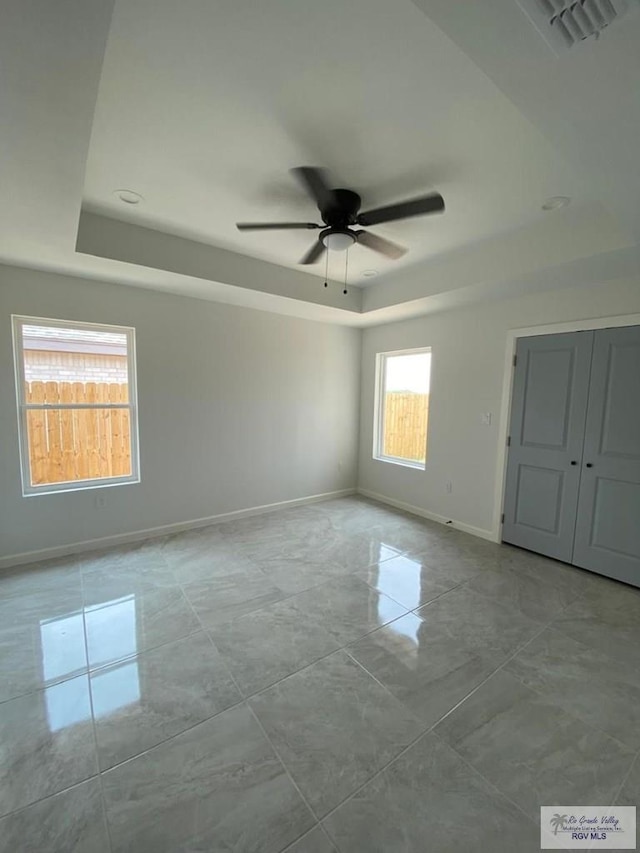 unfurnished room featuring a raised ceiling, plenty of natural light, and ceiling fan