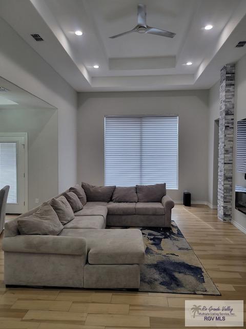 living room featuring ceiling fan, light wood-type flooring, a fireplace, and a tray ceiling