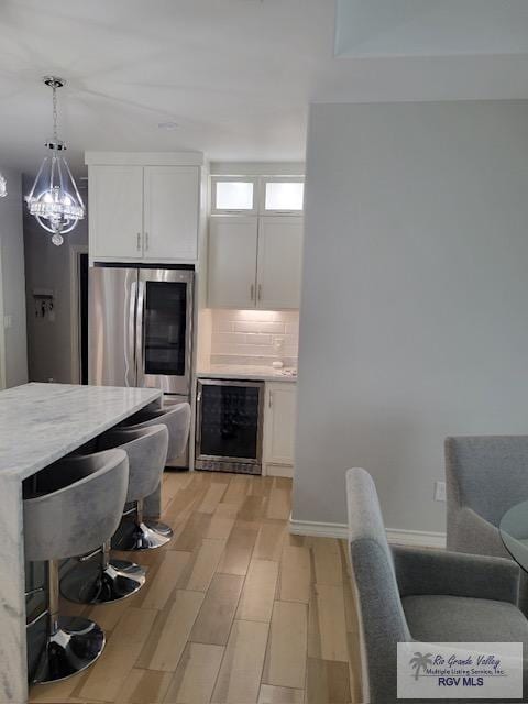 kitchen featuring light wood-type flooring, tasteful backsplash, white cabinets, wine cooler, and hanging light fixtures