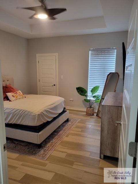 bedroom featuring a raised ceiling, ceiling fan, and light wood-type flooring