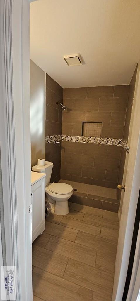 bathroom featuring hardwood / wood-style flooring, vanity, toilet, and a tile shower