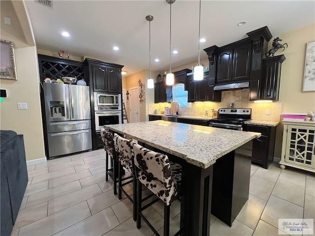 kitchen featuring light stone countertops, stainless steel appliances, decorative light fixtures, decorative backsplash, and a kitchen island