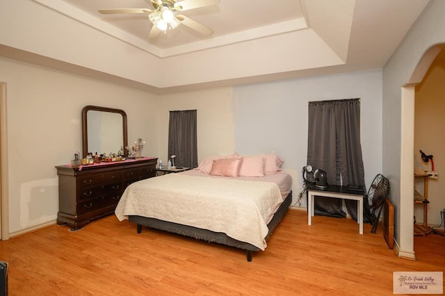 bedroom with light wood-type flooring, a raised ceiling, and ceiling fan