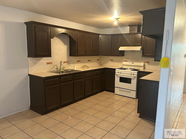 kitchen with tasteful backsplash, light countertops, white gas stove, under cabinet range hood, and a sink