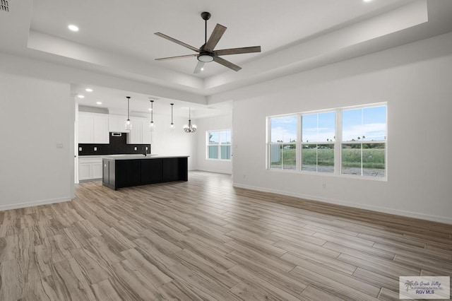 unfurnished living room with ceiling fan with notable chandelier, light hardwood / wood-style floors, and a raised ceiling