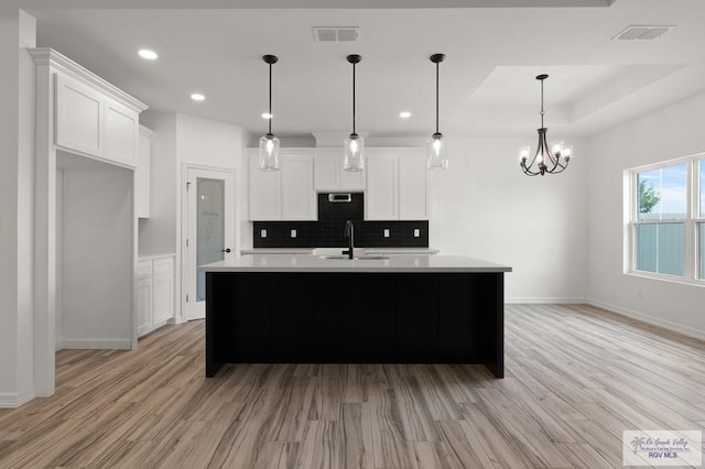 kitchen featuring light wood-type flooring, decorative light fixtures, white cabinetry, and sink