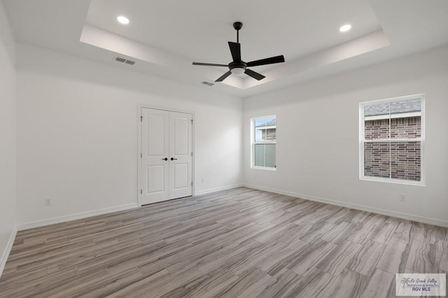 unfurnished room featuring light wood-type flooring, a raised ceiling, a wealth of natural light, and ceiling fan