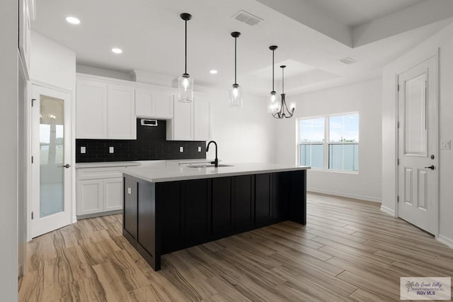 kitchen featuring sink, light hardwood / wood-style floors, white cabinetry, and an island with sink