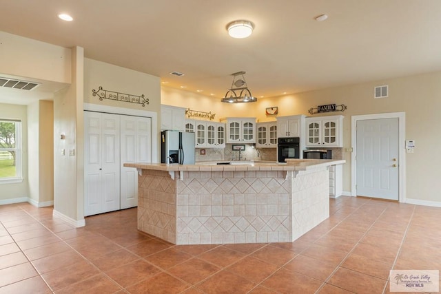 12612 E Clark Rd, La Feria, TX 78559 - kitchen featuring stainless steel refrigerator with ice dispenser, black oven, light tile patterned flooring, backsplash, and tile countertops