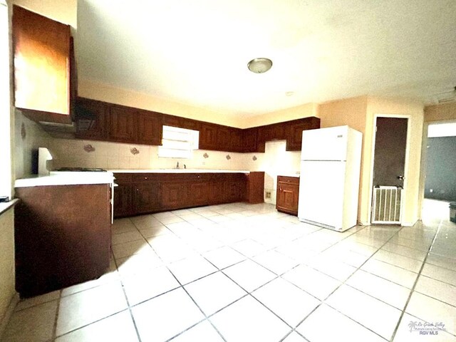 kitchen with light tile patterned floors, dark brown cabinetry, white fridge, and sink