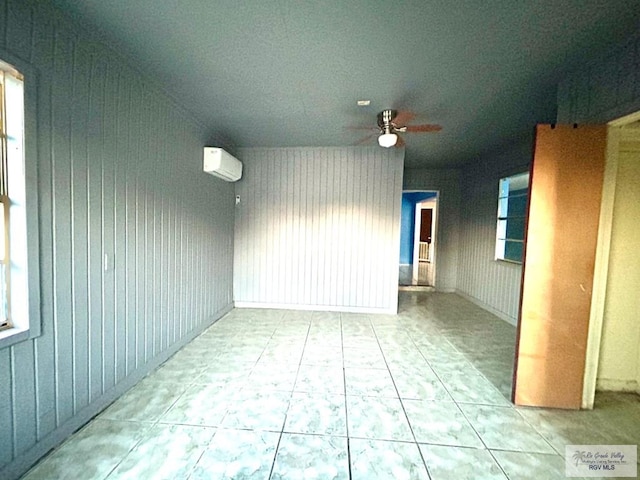 tiled empty room featuring a wall unit AC, a wealth of natural light, ceiling fan, and wood walls