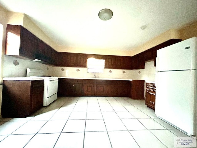 kitchen featuring dark brown cabinets, white appliances, sink, and light tile patterned floors