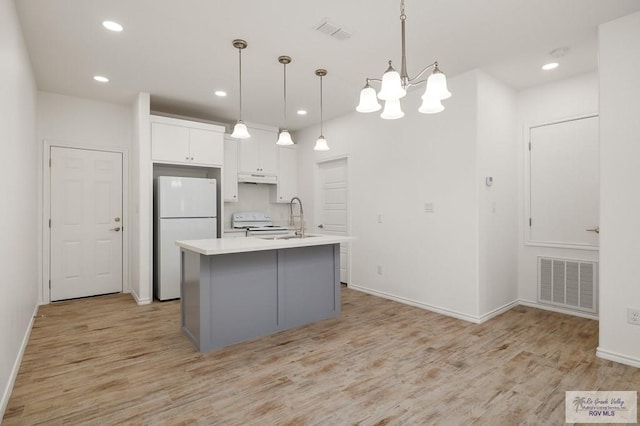 kitchen with white cabinetry, light hardwood / wood-style flooring, pendant lighting, white appliances, and a kitchen island with sink