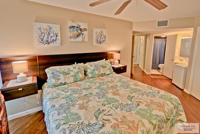 bedroom featuring hardwood / wood-style floors, ceiling fan, stacked washer / dryer, and connected bathroom