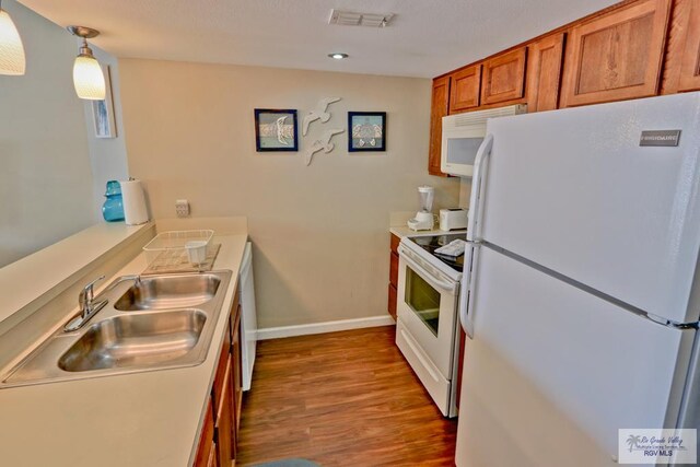 kitchen featuring sink, white appliances, hanging light fixtures, and light hardwood / wood-style flooring