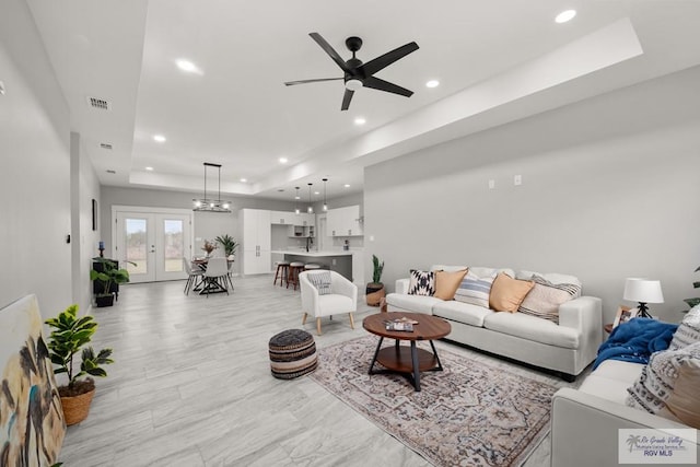 living room featuring a tray ceiling, ceiling fan, and french doors