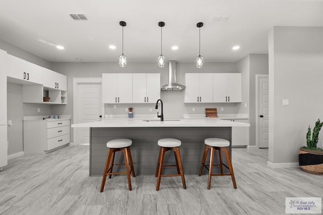 kitchen with sink, a kitchen island with sink, wall chimney range hood, and white cabinets