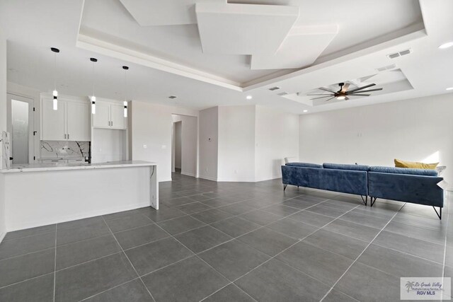 473 Santiago St, La Feria, TX 78559 - unfurnished living room with visible vents, dark tile patterned flooring, a ceiling fan, a tray ceiling, and baseboards
