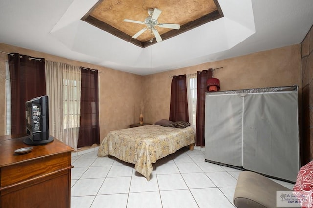 bedroom with light tile patterned floors, a tray ceiling, and ceiling fan