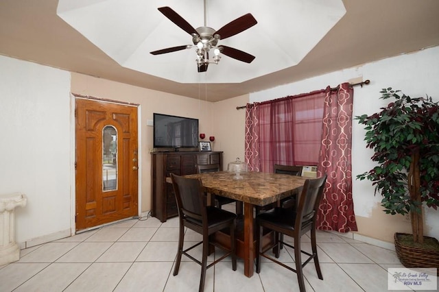 dining area featuring ceiling fan, light tile patterned flooring, and a tray ceiling