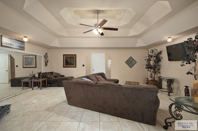 living room with a raised ceiling and ceiling fan