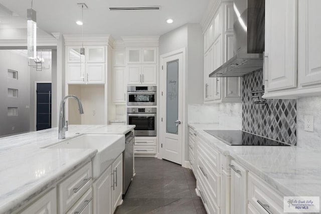 kitchen featuring wall chimney range hood, hanging light fixtures, light stone countertops, white cabinetry, and stainless steel appliances