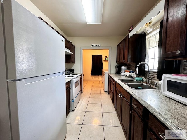 kitchen featuring dark brown cabinetry, white appliances, a sink, and light tile patterned flooring