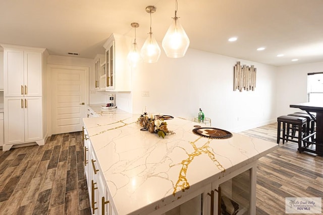 kitchen with white cabinetry, dark hardwood / wood-style floors, light stone counters, and hanging light fixtures