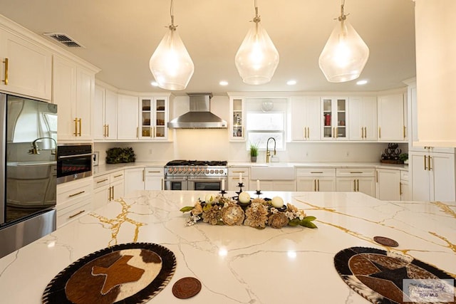 kitchen featuring light stone counters, wall chimney range hood, hanging light fixtures, and appliances with stainless steel finishes