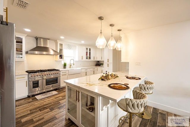 kitchen with hanging light fixtures, white cabinetry, appliances with stainless steel finishes, and wall chimney range hood