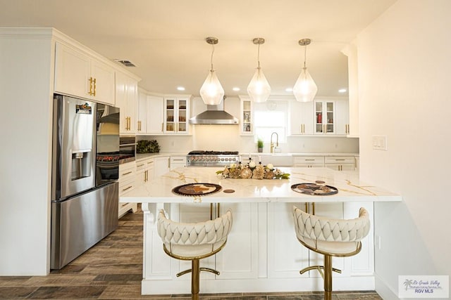 kitchen featuring wall chimney exhaust hood, stainless steel fridge, a breakfast bar, and white cabinets