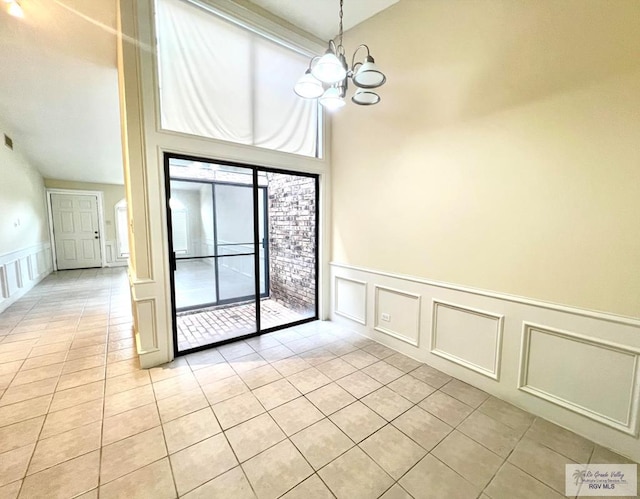 tiled empty room featuring a towering ceiling and a chandelier