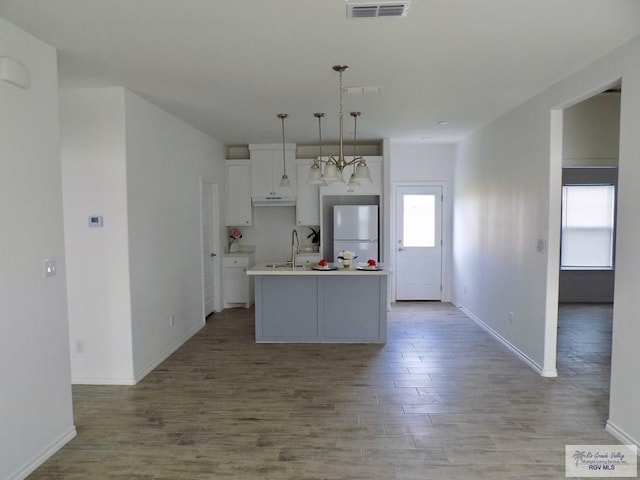 kitchen featuring light hardwood / wood-style flooring, white fridge, white cabinetry, hanging light fixtures, and an island with sink