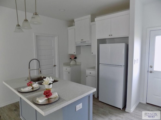 kitchen featuring white refrigerator, white cabinetry, hanging light fixtures, and an island with sink